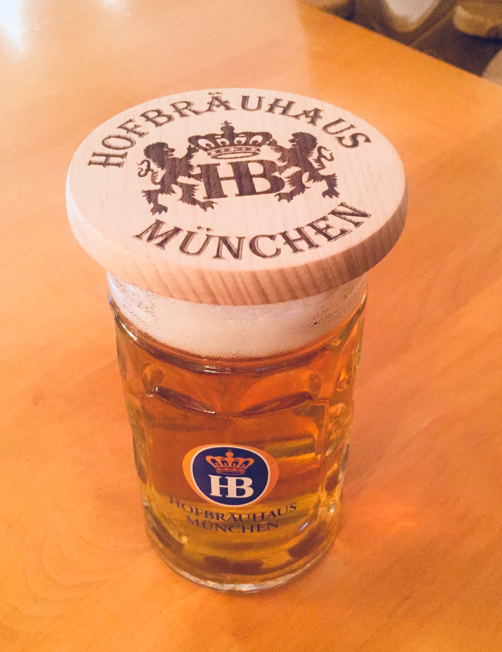 Geschenkpaket Biergarten Holzdeckel mit Hofbräuhaus München Logo auf einem gefüllten Bierkrug mit HB-Emblem.